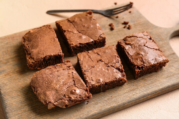 Wooden board with pieces of tasty chocolate brownie on beige background, closeup