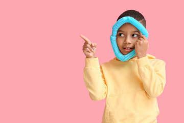 Little African-American boy with blue Pop Tube pointing at something on pink background