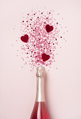 Creative trendy flat lay with pink heart shaped confetti poured out of champagne bottle on pastel...