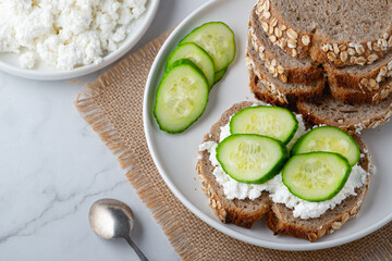 Slices of rye bread with cottage cheese and cucumbers on white background..