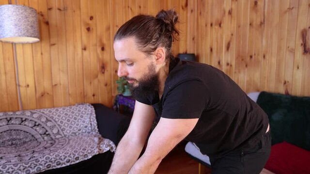 Slow mo movie, as a Shiatsu practitioner with beard and hair bun is seen gently swaying body and using arms to apply pressure to a client off camera.