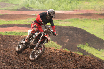 An athlete on a motorcycle rushes along a dirt track. The motorcycle and its equipment are in the...