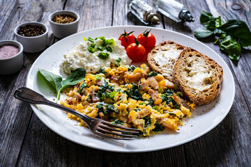 Breakfast - scrambled eggs with bacon, cottage cheese  and vegetables on wooden table
