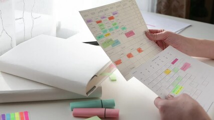 Scheduling and planning the week. Student time management. Women's hands write the schedule on a piece of paper and mark with a marker on a white table on a sunny day. Side view.