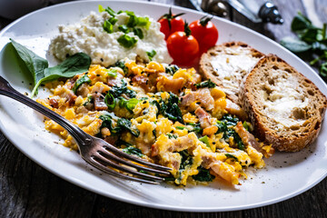Breakfast - scrambled eggs with bacon, cottage cheese  and vegetables on wooden table
