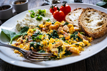 Breakfast - scrambled eggs with bacon, cottage cheese  and vegetables on wooden table
