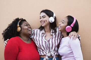 Happy multiracial friends having fun listening music with wireless headphones outdoor - Young...