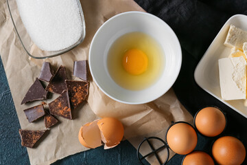 Bowl with fresh egg and ingredients for preparing chocolate brownie on black background