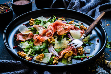 Tasty salad - prosciutto crudo, parmesan and fresh, green vegetables on wooden table
