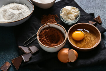 Bowl with cocoa powder and ingredients for preparing chocolate brownie on black background