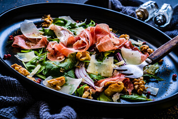 Tasty salad - prosciutto crudo, parmesan and fresh, green vegetables on wooden table
