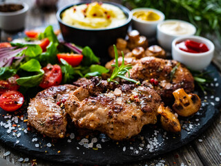 Fried pork steaks with potato puree and vegetable salad served on black stone plate on wooden table

