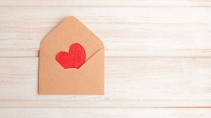 Top view craft envelope with a red felt heart inside on a light wooden background. Copy space