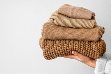 Woman with stack of beige sweaters near light wall