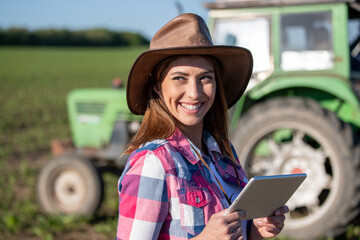 Farmer woman with tablet in front of tractor