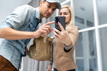 Fast and reliable service. Cheerful young delivery man giving a cardboard box to young woman while standing at the entrance of her apartment