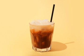 Glass of White Russian cocktail on yellow background