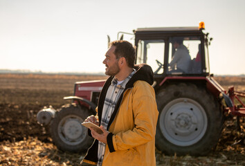 Farmer with tablet in field with tractor in background