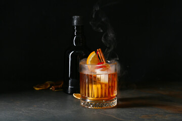 Glass of tasty Old Fashioned Cocktail and bottle with whiskey on black background