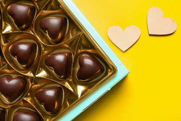 Box with tasty heart-shaped candies on yellow background, closeup