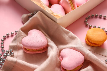 Tasty heart-shaped macaroons and beads on pink background, closeup
