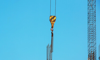 Hooks hanging from large crane chains descending from above. Blue sky background