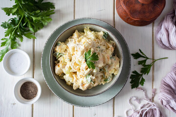 Lunch dish: delicious salad with boiled fish, vegetables, fresh herbs and mayonnaise in a gray plate on a white background. Top view