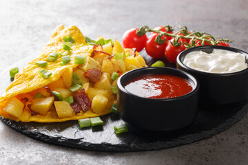 German Bauernomlett omelette with fried potatoes and bacon served with sauces close-up on a slate board on a concrete table. horizontal