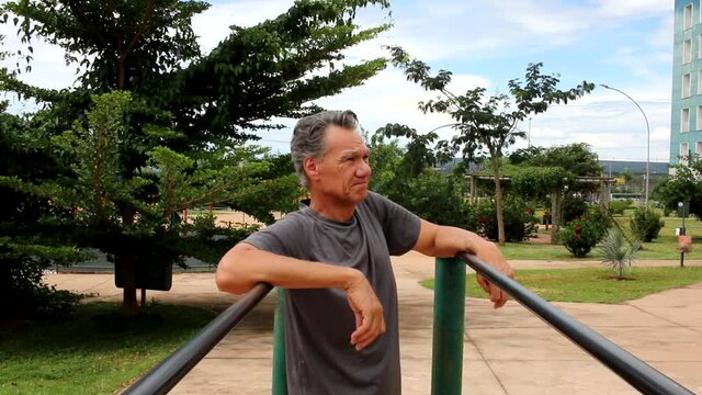 Mature man in Deep thought at a Park Leaning against Some Parallel Bars