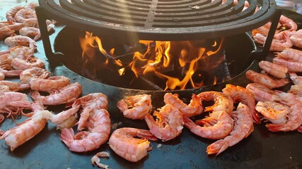 Close up footage of process of grilling fresh king prawns on brazier with hot flame at summer days, a hand in rubber gloves lays out king prawns on a hot iron surface, fresh seafood,