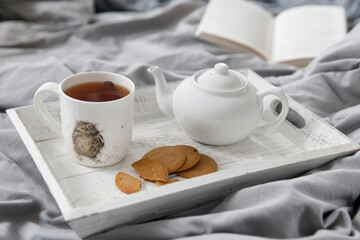 interior and home coziness concept. Top view. A cup of tea, a teapot with herbal tea, sugar bowl on a wooden tray on the bed. Porcelain cup with a drawing 