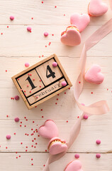 Calendar with date of Valentines Day and tasty macaroons in heart shape on light wooden background