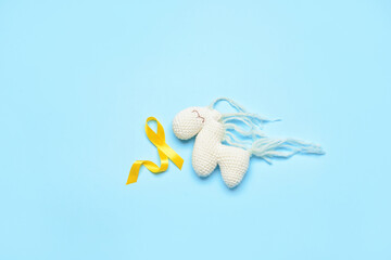 Golden awareness ribbon and toy horse on blue background. International Childhood Cancer Day