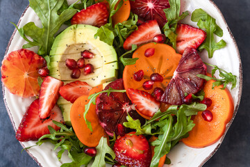 Healthy vegetarian buddha bowl salad with blood orang ,persimmon, arugula, avocado and pomegranate seeds.