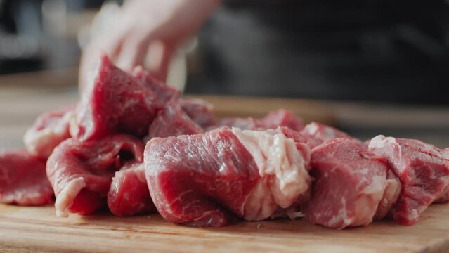 Close up selective focus shot of butcher putting pieces of raw beef meat on wooden cutting board