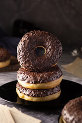 Stacked chocolate glazed donuts on a sleek black plate with a dark textured backdrop.