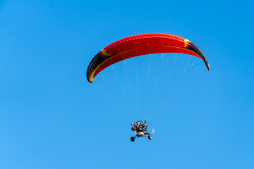 View from below of a paramotor vehicle flying over a clear blue sky