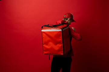 Delivery employee man in red t-shirt uniform work as dealer courier and hold red thermal food bag with food isolated on white background studio. Service concept.