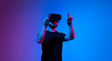 Young man uses virtual reality headset. Cheerful bearded man in t-shirt moving hands and using VR...