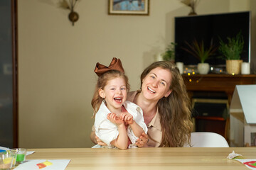 Portrait happy smile family. Mom and daughter at table look at cameras. two sisters laugh At home room and laugh. Place for text. childhood. Caucasian woman and girl in frame. Nanny child Babysitter.