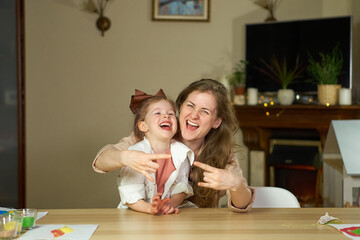 Portrait happy smile family. Mom and daughter at table look at cameras. two sisters laugh At home room and laugh. Place for text. childhood. Caucasian woman and girl in frame. Nanny child Babysitter.