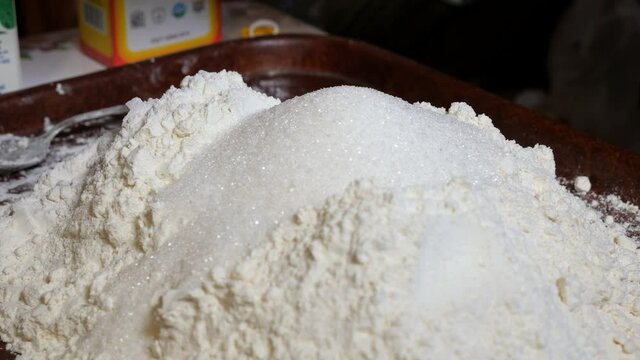 Adding granulated sugar and vegetable oil to flour for baking homemade balls of kolobok. Mixing ingredients with a metal tablespoon.
