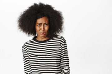 Fototapeta na wymiar Portrait of Black woman staring with aversion and dislike, cringe from smth bad, awful disgusting taste, standing over white background