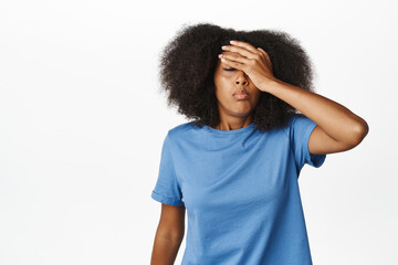 Fototapeta na wymiar Embarrassed and distressed young african american woman facepalm, facing failure or disappointment, looking upset, standing over white background