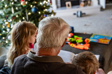 Grandpa reading a storybook to two grandkids sitting on his lap
