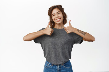 Portrait of young smiling woman showing thumbs up, good, like, approval gesture, satisfied with smth, recommending store or product, white background