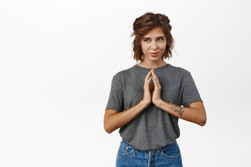 Sneaky young woman planning, scheming something devious, steeple fingers and smirking pleased, has an idea, plan, standing over white background with cunning smile