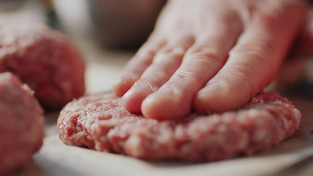 Close up shot of hand pressing raw burger patty on baking sheet before cooking