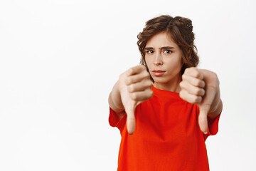 Young woman express dislike, showing thumbs down, disapprove, prohibit something, standing in red...