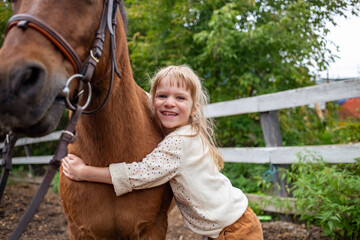 little girl hugs pony horse in corral and laugh happy